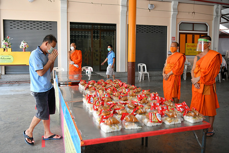 A man greets a monk before receiving a free meal at the Wat Arun Buddhist temple in Bangkok.
The Wat Arun temple is providing two free meals a day for people in need whose livelihood has been affected due to the emergency regulations enforced in Thailand to control the spread of coronavirus.