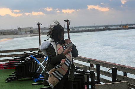 A Palestinian woman checks her phone in a coffee shop during a dust storm with strong winds at sunset.