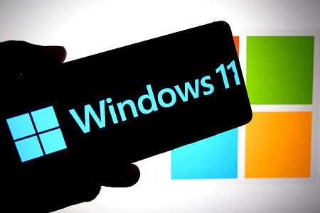 In this photo illustration, a Windows 11 logo is seen displayed on a smartphone with a Microsoft logo in the background.