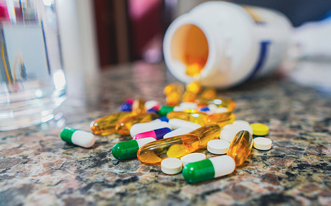 In this photo illustration, several pills on the table next to a glass of water.