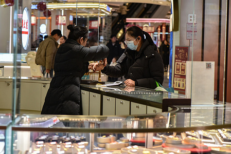 A customer tries on jewelry with the help of a salesperson at a bustling jewelry counter in Fuyang Wuyue Mall.