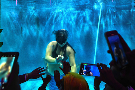 Visitors watch & seen taking photos of an underwater mermaid performance at a Fair of Baruipur. The indoor mermaid performance is staged in the 6-meter-long transparent mermaid tank.