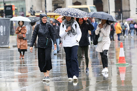 Members of public shelter under umbrellas during wet weather in central London. The Met Office forecast temperatures in London to reach 20 degrees Celsius on Saturday following rain, thunder and lighting this week.