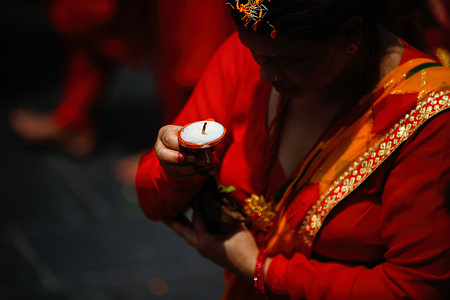 A Nepalese Hindu woman prays while holding a lit candle during the Teej festival inside Pashupathinath Temple in Kathmandu. Married and unmarried women observe fasting. Married women abstain strictly from food and drinks, believing their devotion to god will be blessed with longevity, peace, and prosperity for their husbands and family. Unmarried women observe the fast with the hope of being blessed with a good husband by praying, singing, and dancing.