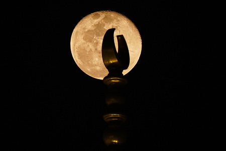 The full moon rises above the crescent of one of the minarets of the Grand Mosque.