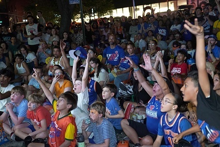 A large crowd gathers and cheers outside a corner Deli at 10th Ave. and 45th Street that hosts a watch party for the New York Knicks Game 5, as they win the NBA Championship for 2026 against the San Antonio Spurs.
