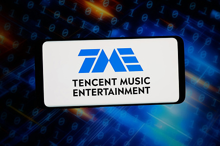 In this photo illustration, the logo of Tencent Music Entertainment Group (TME) is displayed on a smartphone in front of abstract background on computer screen.