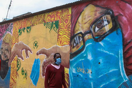 A man wearing a face mask walks past a mural depicting the importance of wearing a face mask by the Mathare Roots Society initiative group that uses the graffiti form of creative art to inform and sensitise the residents of Mathare slums.
