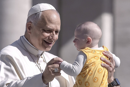 Pope Leo XIV greets a child as he arrives for his weekly general audience in St. Peter's square at the Vatican.