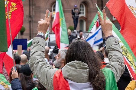 A supporter makes gestures as she celebrates the unconfirmed news of the Ayatollah's Ali Khamenei's death. Manchester centre saw hundreds of pro regime Iranians celebrate after rumors of Ayatollah's Ali Khamenei's death spread amongst the crowd. The pro regime crowd had gathered to show support for the action taken by the USA ordered by Donald Trump. Supporters opened a bottle of 'Champagne' and sprayed the crowd when the unconfirmed report of the Ayatollah's death was announced over the speaker systems. Flags of the USA, UK and Israel as well as the prerevolutionary Iranian flag were carried by supporters.