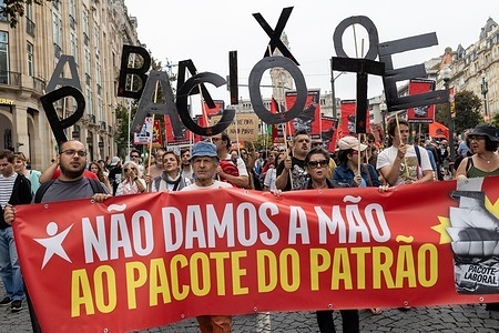 Protesters hold individual letters spelling out the phrase “Abaixo o pacote” (Down with the package) during a national general strike, expressing opposition to the government’s proposed labor reform package. Demonstrators gathered at Praça da Batalha and Avenida dos Aliados for a national general strike. Union groups, workers, and supporters marched with banners, flags, and handwritten signs criticizing the government’s proposed labour reforms and calling for improved working conditions, higher wages, and stronger public services. The protest featured megaphones, flares, and visual messages reflecting broad mobilization across the city.