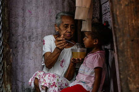 A woman in extreme poverty give a spoon of soup to her grandchild inside her house. The food was provided by a non profit social organization that supports people in extreme poverty.