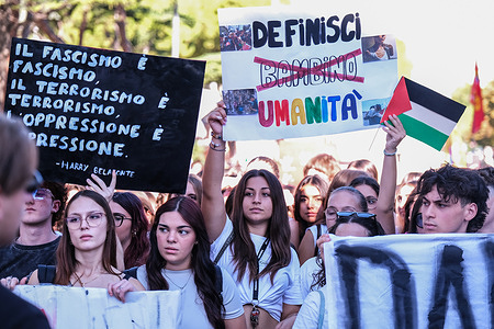 A young man carries a sign quoting Harry Belafonte: "Fascism is fascism, terrorism is terrorism, opposition is opposition," while a young woman holds a sign reading "Definisci bambino umanità," a metaphorical call to reflect on the meaning of "child," during the national strike. Students, trade unions, and citizens marched through the city streets to demonstrate in support of Palestine against the genocide and in solidarity with the Global Sumud Flotillia.