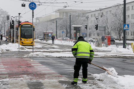 A man clears snow at a pedestrian crossing in the Praga Północ district. Snowfall overnight covered the city streets in Warsaw. Pedestrians and commuters move through fresh snow as winter weather settles in the capital.