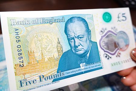 In this photo illustration, a hand holds a five pound banknote of the Bank of England with Winston Churchill's portrait, and other banknotes are behind.