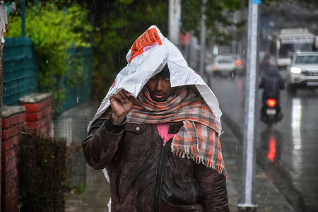 A labourer covers his head with a polythene bag as he walks through a street during the rainfall in Srinagar.
