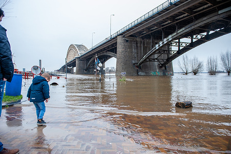 A little boy is seen splashing water with his shoes near Waal bridge.
The water in the rivers is rising sharply. During morning, high water was expected in both the Meuse and the Rhine. Even if the water levels were not so high as last January, people gathered around the waalkades to see the high water levels. This time around it reached around 13 meters above NAP this weekend. NAP is the base used to measure how high or low water levels are.