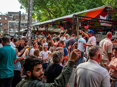 People are seen enjoying the music in a crowded square. The Vierdaagsefeesten (Dutch for Four Days Festival) event is held simultaneously with the International Four Days Marches. Every year, this event presents a versatile program with more than 1,000 acts on over 45 stages, all of which are completely free, attracting over 1.5 million people to the inner city of Nijmegen.
