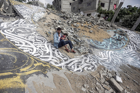 A Palestinian man holds his child amidst a calligraphy artwork drawn by artist Ayman Al-Husari (not pictured), on the ruins of a house destroyed by Israeli airstrikes during the May 2023 conflict, in Beit Lahiya in the northern Gaza Strip.