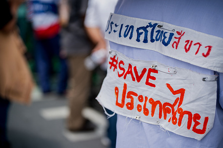 A protester is seen with a sign reading "Thailand white (pure)" and "#SAVE Thailand" during a demonstration. The People and Student Network for the Reform of Thailand staged a protest near the Government House in Bangkok, calling for Prime Minister Paetongtarn Shinawatra to resign after the leak of her phone call with Cambodian Senate President Hun Sen. The demonstration occurred following rising Thai-Cambodian border tensions and accusations that Paetongtarn compromised national security.