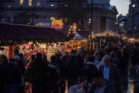 The crowd walks by the Trafalgar Square Christmas market in London. The Trafalgar Square Christmas market is located outside the National Gallery, London. The market offers a festive atmosphere with twinkling lights and beautiful traditional decorations.