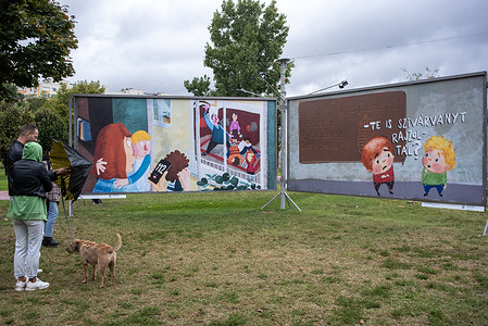 A couple looks at the posters in Budapest. The left poster shows domestic violence at the neighbor family. The right one shows the 'Institute of the Abused Children with Gender Propaganda'. One child asks the other like 'Did you draw a rainbow as well?' The 24th ARC (FACE) open-air billboard exhibition is open to the public in Budapest, Hungary. It is about the freedom of creativity. Exhibition is an ironic, provocative, humorous and very political poster event.