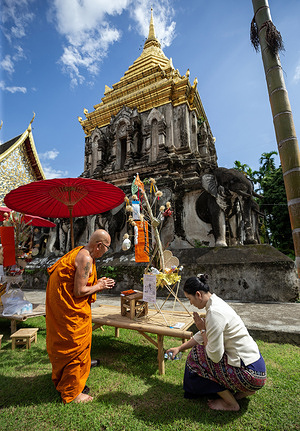 A monk is offering blessings to a devotee attending the festival at Wat Chiang Man. "Tan Kuay Salak" is a tradition of the Lanna people to make merit for the deceased. It is held at the end of the rainy season (September-October). Villagers prepare offerings such as food, sweets, fruits, and daily items, placing them in containers called "Kuay Salak," which are made from woven materials. These are then randomly drawn and given to monks or recipients of merit. This ceremony represents shared merit-making between the living and the deceased, promoting blessings and fostering unity within the community.