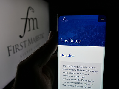 In this photo illustration, a person is holding a smartphone with the webpage of mining company First Majestic Silver Corp. on screen in front of logo.