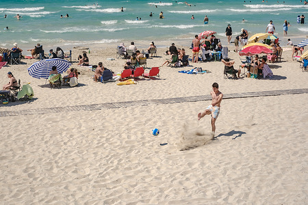 A young man is playing soccer on the beach. People enjoy the summer season at Ilıca Beach in Cesme, Izmir, Turkey. Visitors swim, sunbathe and relax along the shoreline as warm weather and the peak holiday season attract large numbers of local and international tourists. Known for its shallow, turquoise waters, İlica Beach remains one of the Aegean coast's most popular seaside destinations.