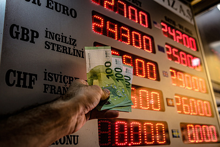 A man is holding cash in his hand, with the exchange rates visible in the background. The dollar reached a historic high at 23.22 Turkish Liras while Euro broke a record at 25 Turkish Liras. Experts say that economic trouble is at the door. In the face of this rise, people have been at exchange offices exchanging dollars and euros.