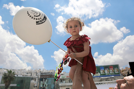 A Palestinian girl holds a balloon in the central market of Nablus in the West Bank, in preparation for Eid al-Adha. Palestinians celebrate the holiday and prepare for it by purchasing essential supplies. Shoppers flock to the Nablus market despite the difficult economic conditions and the financial blockade imposed on the Palestinian Authority areas under the leadership of President Mahmoud Abbas.