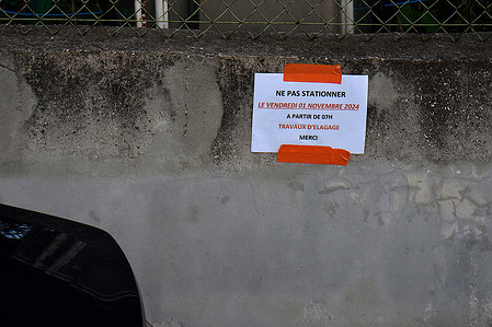 A pruning information note is seen on a wall near a parked car. In order to ensure the parking and circulation of its vehicles near the construction site, a tree pruning company informs by means of a notice of the need not to park near the construction site.