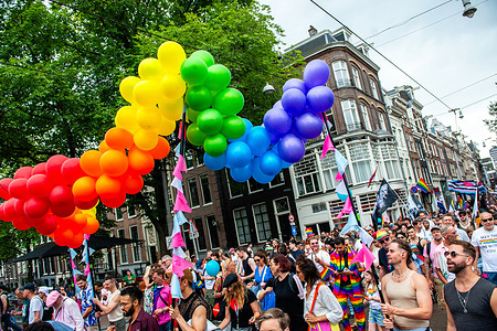 Participants are seen dancing below a rainbow of balloons. The annual Pride Parade for the global rainbow community took place in Amsterdam. People and organizations came together to advocate for the acceptance and equality of LGBTQA+ individuals worldwide.