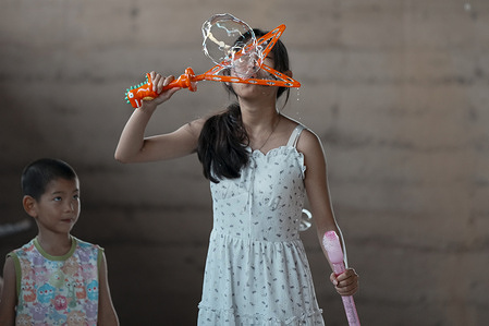 A girl seen playing with a bubble machine in the street park.
