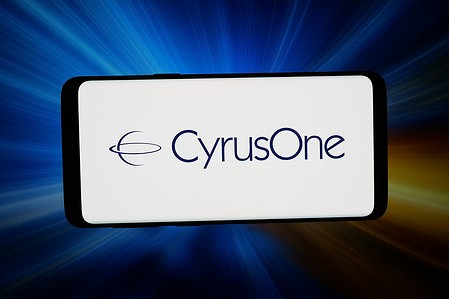 In this photo illustration, the logo of US data center company CyrusOne Inc. is displayed on a smartphone in front of abstract background on computer screen.