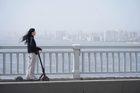A young woman seen riding an electric scooter (e-scooter) on the pedestrian sidewalk of the Saratov Bridge over the Volga River.