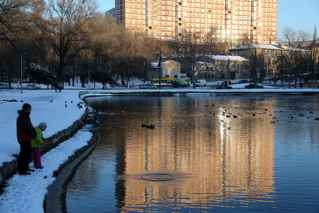 An adult and a child stand by the water at Dyukovsky Park while enjoying the cold winter snowy weather.