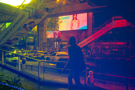 The window of the shopping mall Siam Center reflects people and Rama 1 street in Bangkok.