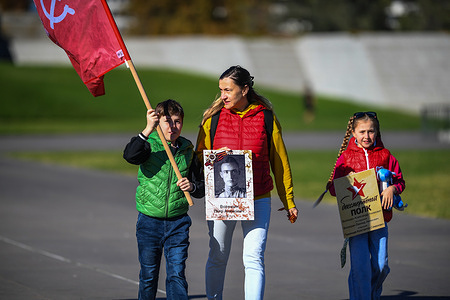 A woman with children walks with "The Immortal Regiment" posters seen at the Shrine of Remembrance commemorating Victory Day.