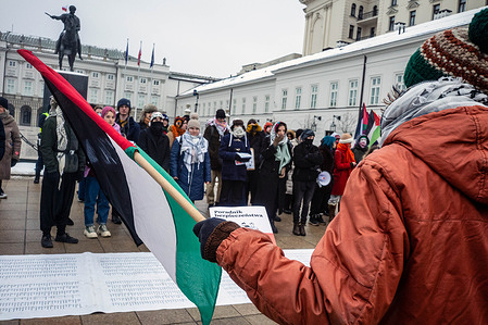 A protester talks to the demonstration while holding a Palestine flag and a Polish "Safety Guide" booklet recently distributed by the Polish government detailing what to do in the event of conflict or emergency. On the afternoon of Sunday 25th of January, pro-Palestinian and anti-genocide demonstrators gathered at the Presidential Palace in Warsaw to mark the 2nd anniversary of the Israeli murder of five-year-old Hind Rajab. After speeches, protesters marched behind a bullet-ridden Kia Picanto to the American embassy, then on to the Parliament of the Republic of Poland. On the 29th of January 2024, after her family's car was fired upon by Israeli forces while fleeing, Hind Rajab survived for hours in her father's Kia Picanto, calling for help while trapped with deceased relatives. She was subsequently killed alongside paramedics attempting to rescue her.