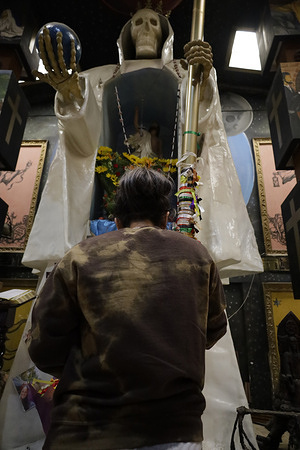 A person seen worshiping Santa Muerte and the Black Angel (The Devil) at a temple where people gather to give thanks for favors received on the eve of Holy Week. According to popular belief, Santa Muerte is considered among the "dulia (tribute to angels and saints) as an intercessor and mediator between the earthly and the divine, life and death, heaven and earth." Meanwhile, the Black Angel (The Devil) is one of the representations of Lucifer. Both cults are condemned by the Catholic Church and other religious denominations.