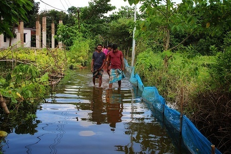 People walk through a submerged road at Demra area near Dhaka.
As many as 20 districts – including the latest additions Chandpur, Brahmanbaria, and Naogaon – have so far been hit with the worsening flood situation across Bangladesh and many more areas might be inundated if the situation does not improve soon, said Flood Forecasting and Warning Centre (FFWC).