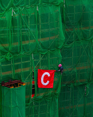 A construction worker peeks out from behind green netting covering bamboo scaffolding on a newly constructed building in Quarry Bay.