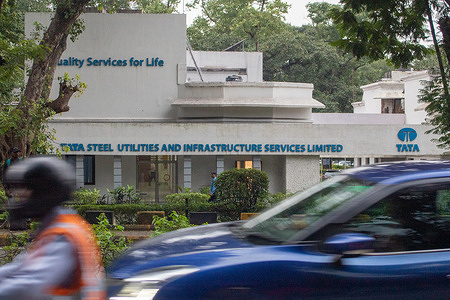 A view of the Tata logo displayed at the Tata Steel Utilities and Infrastructure Services Limited (TUSIL) office, formerly known as Jamshedpur Utilities and Services Company Limited (JUSCO). The UK’s largest steelmaker, Tata Steel, continues to influence industry decisions across both India and the United Kingdom amid major restructuring and labor concerns. Its dominant position includes supplying nearly half of the steel used by UK car manufacturers and operating the country’s only primary steelmaking facility with significant domestic research and development. This status is evolving as Tata Steel undertakes a £1.25 billion transition to low-carbon production using Electric Arc Furnaces, a move that aims to secure its long-term future but raises concerns over job losses linked to the closure of traditional blast furnace operations.