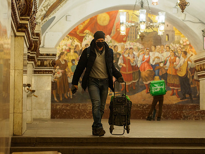 A man wearing a face mask and gloves as a precaution against the spread of coronavirus, pulling a cart at Moscow metro.