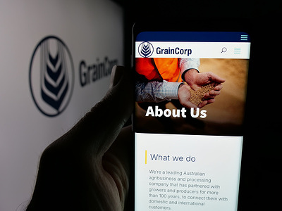 In this photo illustration, a person is holding a smartphone with the webpage of Australian commodity company GrainCorp Ltd. on screen in front of logo.