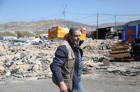 A Palestinian man carries a box of fruits near the fruit and vegetable market after it was demolished by Israeli army bulldozers in the West Bank village of Beita, near Nablus. Israeli forces demolished the Beita fruit and vegetable market, which was built near a settlement road owned by Jewish settlers.