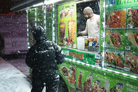 A street vendor, open for business, prepares a person's meal. The northeast U.S. was hit by an intense nor'easter with blizzard conditions, heavy snow and strong winds.