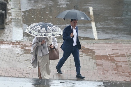 People shelter under umbrellas while walking along the the road during heavy rain in the center of St. Petersburg.
