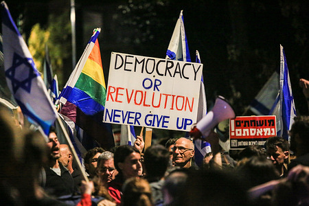 Protesters wave Israeli flags and hold placards expressing their opinion during a demonstration against the Israeli government's controversial justice reform bill outside the prime minister's residence in Jerusalem.